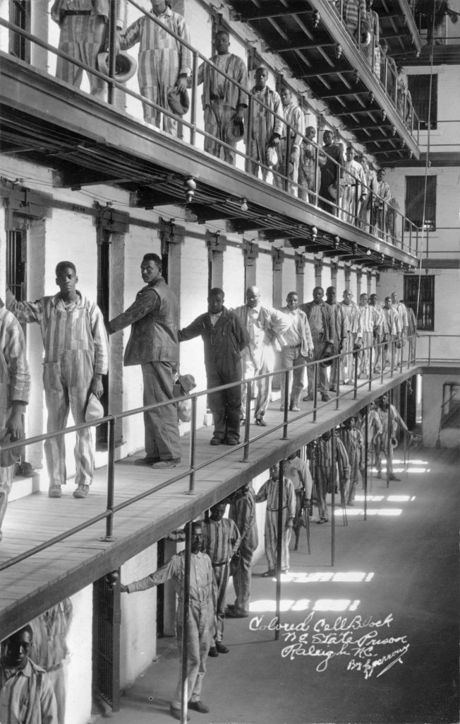 Black and white photograph of the interior of the Black portion of a prion with inmates standing outside their cells