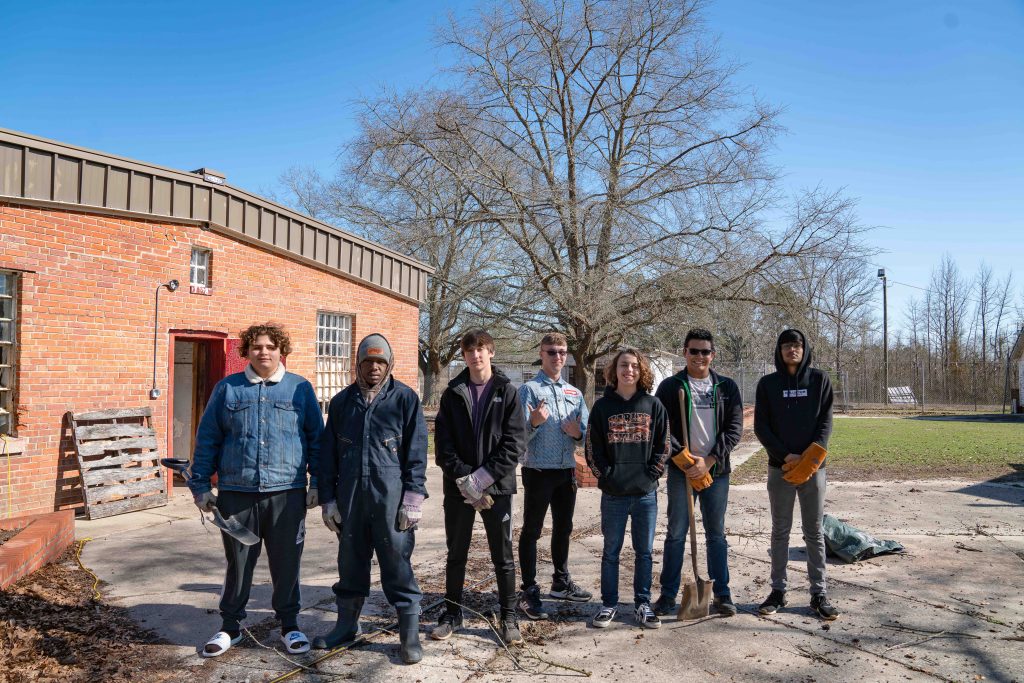 A group of seven youth leaders stand outside and hold shovels.