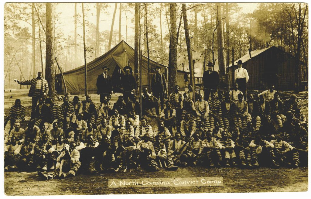 Black and white photograph of a group of prisoners outside in front of a canvas tent. 